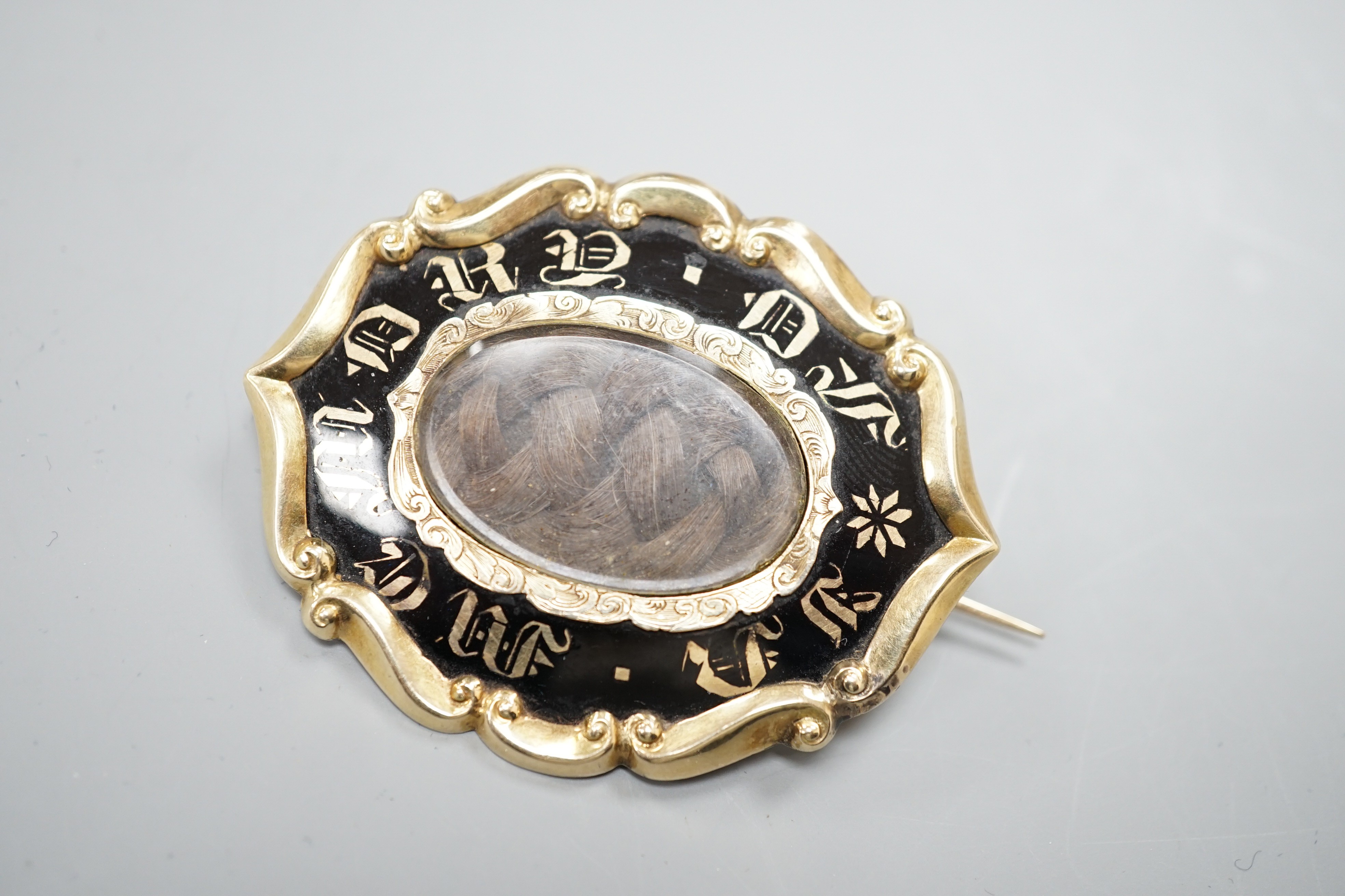 A Victorian yellow metal overlaid and black enamel 'In Memory Of' shaped oval brooch, with central glazed plaited hair panel, 52mm.